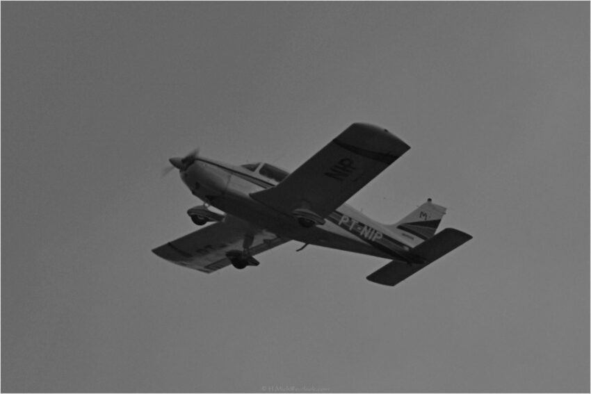 StudioOne Repo – Fotografia PB de um avião voando no céu.