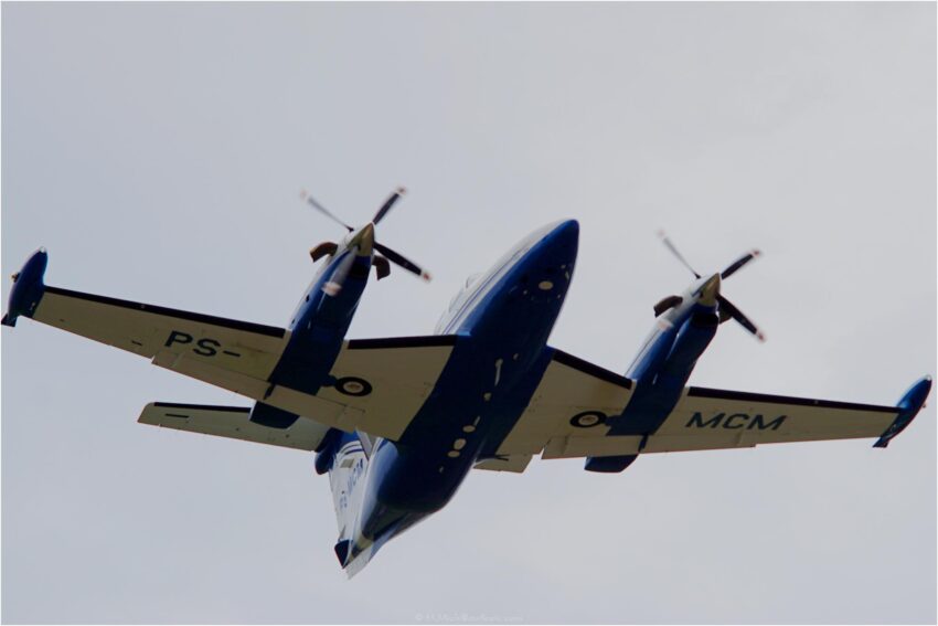 StudioOne Repo – Vista inferior de um avião azul e branco voando no céu.