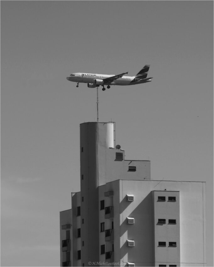 StudioOne Repo – Fotografia PB de um avião voando sobre edifícios.