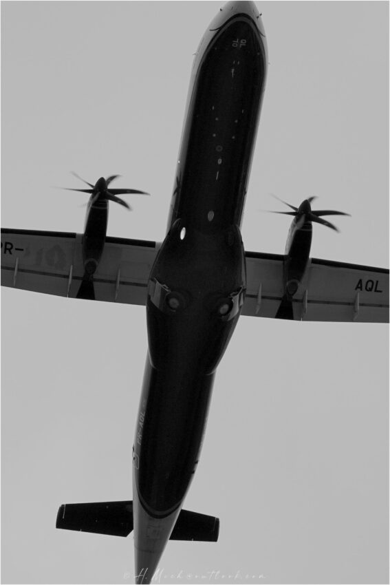 StudioOne Repo – Fotografia PB de um avião voando no céu.