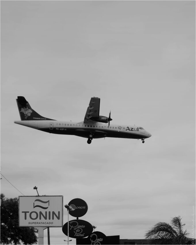 StudioOne Repo – Fotografia PB de um avião voando sobre uma cidade.