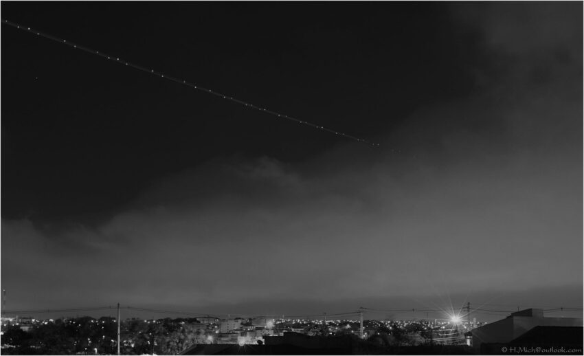 StudioOne Repo – Fotografia PB de um avião voando sobre uma cidade à noite.