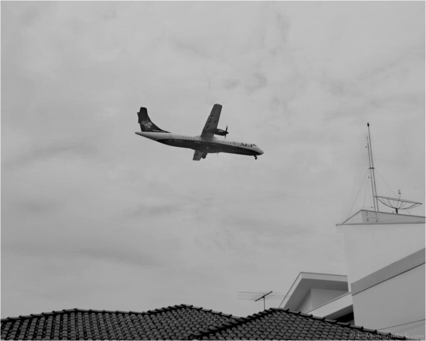 StudioOne Repo – Fotografia PB de um avião voando no céu.